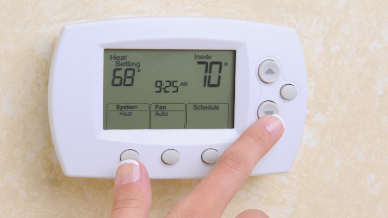Finger adjusting wall-mounted digital thermostat showing 68°F heat setting and 70°F inside temperature.