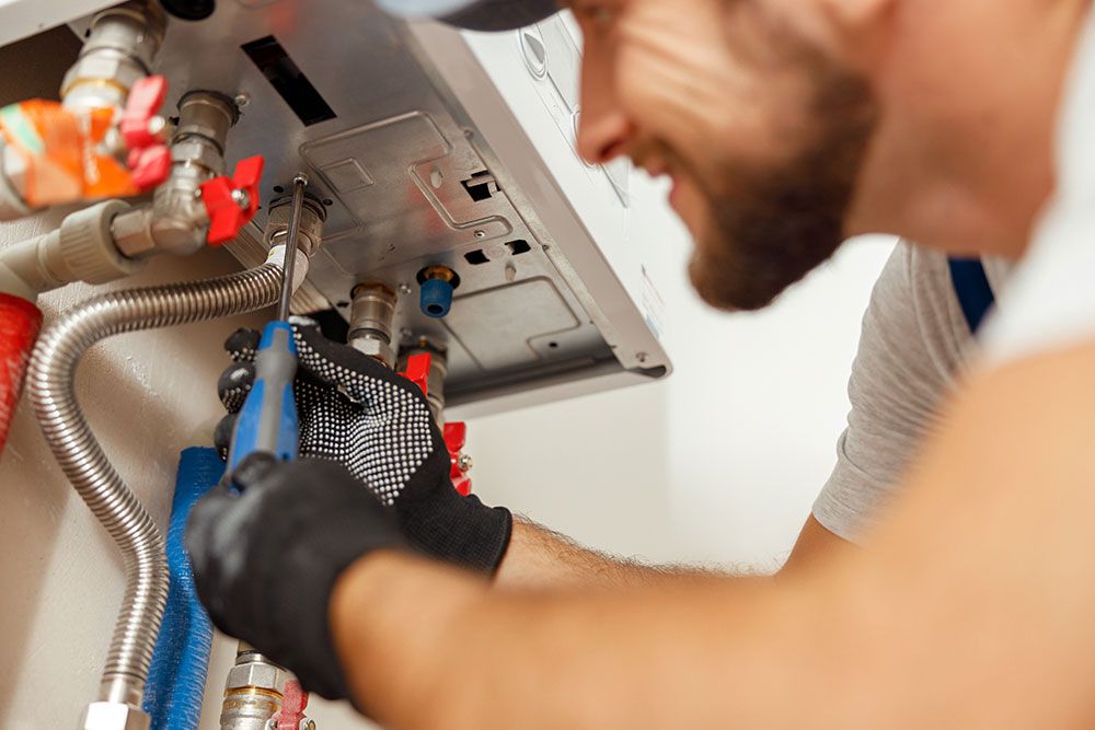 Plumber repairing a water heater using a screwdriver, focusing on pipes and connections.