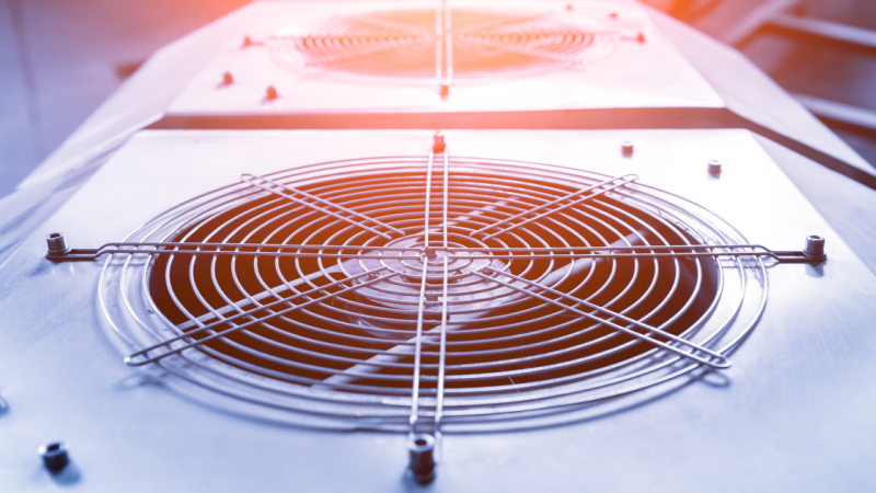 Close-up of industrial cooling fan with metal grille, illuminated by sunlight, illustrating HVAC technology.